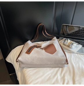 Detail view of large canvas tote bag featuring brown leather straps and front zip pocket