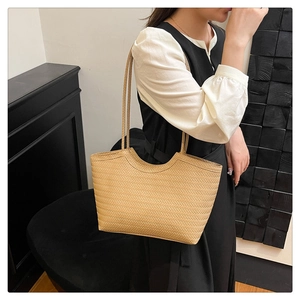 Detail of beige woven tote bag with slim handles shown on a model in a minimalist setting