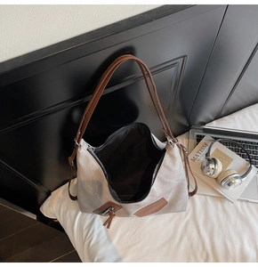 Detail view of large grey tote bag with brown handles and zipper on minimalist desk