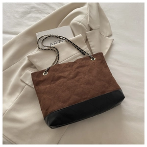 Detalle de bolso tote de ante marrón acolchado con base de cuero negro y cadena de oro