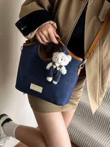 Denim handbag with bear pendant and brown leather handles shown on model in trench coat