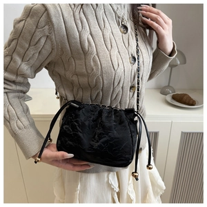 Détail du sac bandoulière noir plissé avec des breloques dorées en métal sur cordon