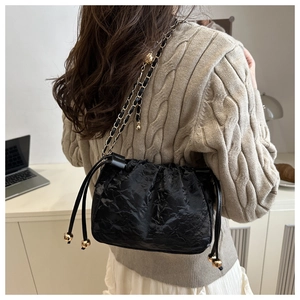 Détail du sac à bandoulière plissé noir avec chaîne dorée sur un pull en maille beige