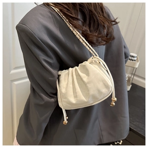 Détail d'un sac seau plissé blanc crème avec bandoulière chaîne et pendentif boule dorée