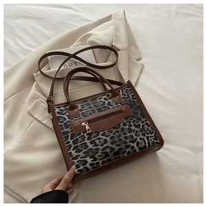 Detail of leopard print handbag featuring a front zipper pocket and brown leather handles