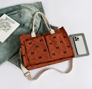 Detail view of brick red corduroy tote bag with black bow pattern and canvas straps