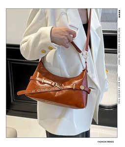 Close-up of caramel leather tote bag with gold eyelets and buckle on white blazer
