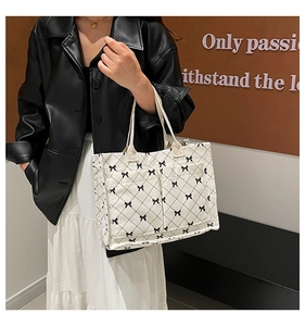 Close-up of a white corduroy tote bag featuring black quilted patterns and bow accents
