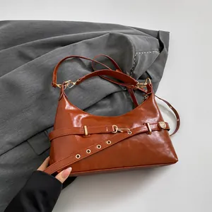 Close-up of brown glossy crescent leather handbag with belt buckle and metallic details