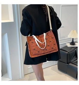 Detail of brick red corduroy tote with black bow prints worn over a black blazer