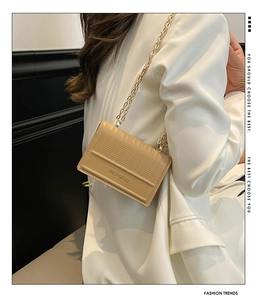Dettaglio della borsa a tracolla beige intrecciata con catena dorata indossata dal modello