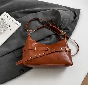 Detail of caramel leather hobo bag with gold buckle on grey blazer backdrop