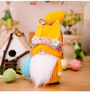 Detail of yellow knitted Easter gnome holding a blue egg with a floral wreath on its hat