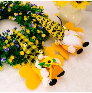 Detail of bee gnomes with striped hats holding sunflower and honey stirrer decorations