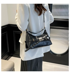 Detail of black glossy shoulder bag with metal grommets and buckle worn by model