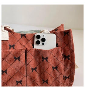 Detail of corduroy tote bag featuring a diamond pattern, bows, and a functional front pocket