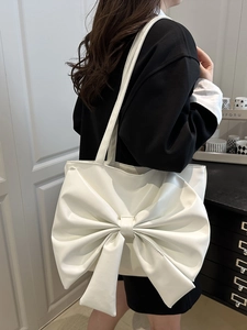 White faux leather tote bag with large 3D bow decoration shown on model shoulder