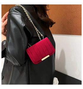 Close-up of red velvet shoulder bag with vertical stitching and gold metal buckle