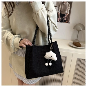 Detail of black quilted tote bag with woven handles and a cute white cloud plush pendant