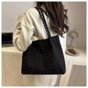 Detail of black textured tote bag with woven handles shown in a lifestyle office setting