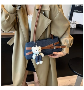 Detail of blue denim baguette bag featuring brown leather straps and a cute plush bear charm