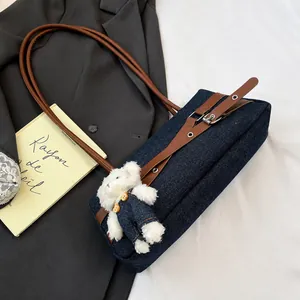 Detail of dark blue denim baguette bag with brown leather strap and plush bear charm