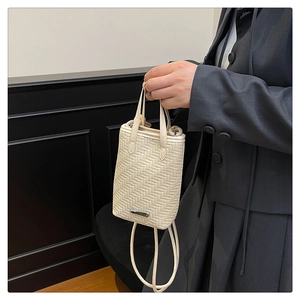 Détail macro du sac à main beige tressé avec plaque métallique et doubles poignées