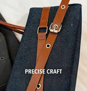 Detail of denim shoulder bag with brown leather strap and silver metal buckle hardware