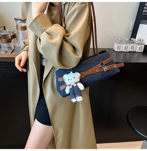 Close-up of denim baguette bag with brown leather straps and a plush bear pendant
