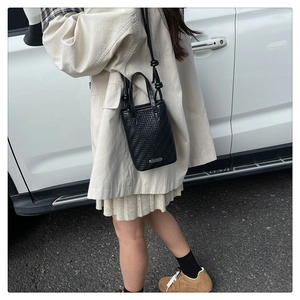 Détail d'un sac seau en cuir noir tressé avec motif en V et base logo en métal