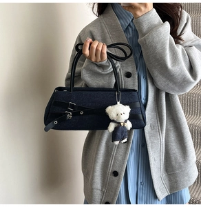Detail of denim baguette bag with black leather straps and a cute white bear charm