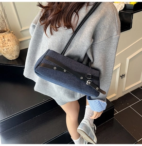 Detail of denim and black leather baguette bag with silver eyelets on a dark staircase