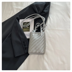Détail d'un mini sac cabas tressé argenté avec bandoulière nouée sur fond minimaliste