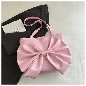 Dettaglio borsa shopper rosa con grande fiocco e trama in pelle opaca su sfondo di tessuto
