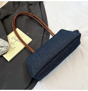 Détail du cabas en denim bleu foncé avec anses en cuir marron sur fond de blazer gris