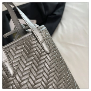 Détail rapproché d'un sac à main tressé argenté avec texture métallique en cuir synthétique
