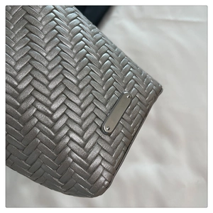 Détail de la texture en cuir tressé argenté et plaque en métal sur le sac à bandoulière