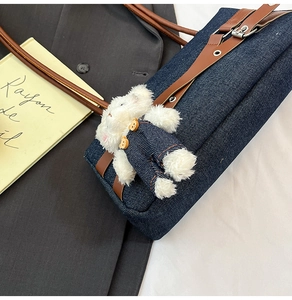 Détail du sac d'épaule en jean avec bandoulière en cuir brun et breloque ours en peluche