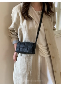 Detail of a black woven crossbody bag with letter embossed pattern and minimalist strap