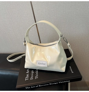 Detail of cream high-gloss handbag with silver hardware resting on a black book