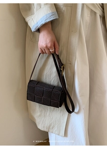 Detail of dark brown woven leather crossbody bag with iconic golden triangle buckle