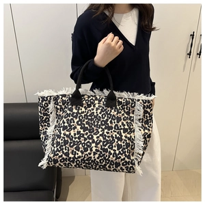 Detail of leopard print tote bag with white fringe trim and black fabric handles