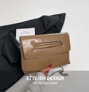Detail of brown PU envelope bag with metal chain strap on grey blazer background