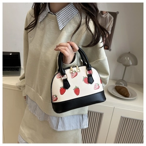 Détail du sac à main coquillage blanc avec motif fraise et finitions en cuir noir