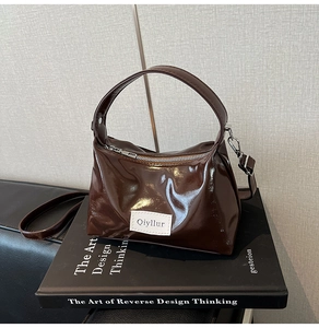 Close-up of a dark brown glossy patent leather hobo bag on a book with silver metal zipper
