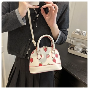 Detail shot of the white shell crossbody bag with strawberry print and gold hardware