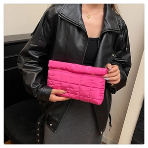 Detail of pink quilted envelope clutch bag with padded texture and metal buckle on model