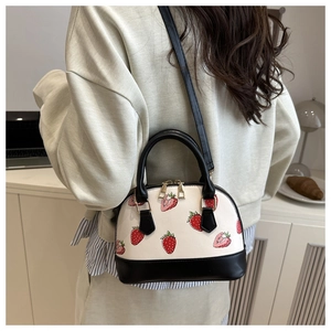 Detailed view of white shell bag with strawberry prints and black leather handles