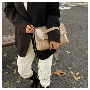 Detail of dark khaki leather envelope bag with silver chain strap on a model outdoors