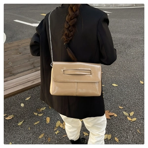 Street style shot of a khaki leather envelope bag with a silver chain strap and top handle